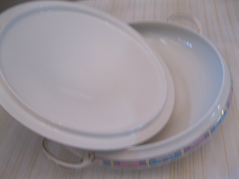 May include: A white oval serving dish with a lid. The dish has a pink and blue patterned border.