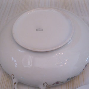 May include: White ceramic serving bowl with a floral pattern and gold trim. The bowl has two handles and a raised center section. The bottom of the bowl has the text "Made in U.S.A."