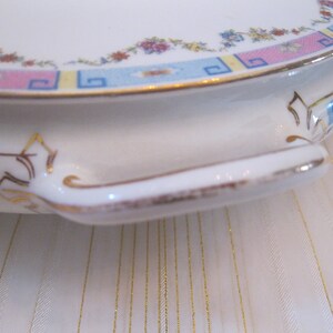May include: A white ceramic serving dish with a gold trim and a floral pattern in shades of pink, blue, and yellow. The dish has a handle on each side.