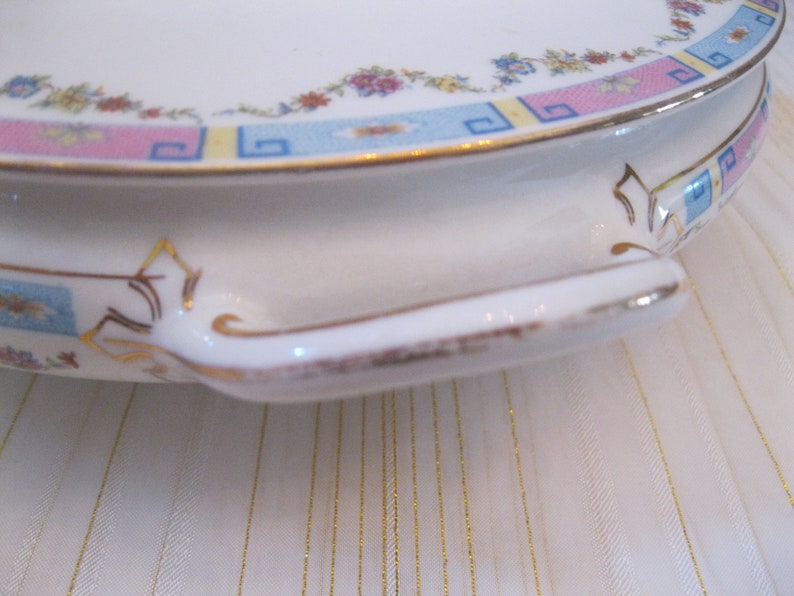 May include: A white ceramic serving dish with a gold trim and a floral pattern in shades of pink, blue, and yellow. The dish has a handle on each side.