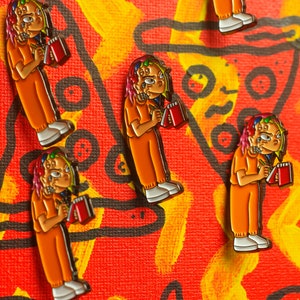 Puede incluir: Cuatro pines de esmalte coloridos con un personaje de dibujos animados con cabello arcoíris que lleva un mono naranja y sostiene un cuaderno rojo. El personaje está escribiendo en el cuaderno con un bolígrafo.