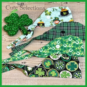 May include: A collection of St. Patrick's Day themed scrub caps in various green patterns, including shamrocks, leprechauns, and plaid. A glittery green shamrock decoration is also present. The text "Cute Selections" is visible.