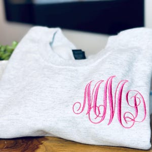 May include: A gray sweatshirt with a pink monogram of the letters "MM" embroidered on the front.