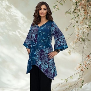 Peut inclure: Une tunique bleue avec un col en V et un ourlet asymétrique. La tunique présente un motif de libellules et de fleurs dans des tons de bleu et de violet. Le modèle porte un pantalon noir.