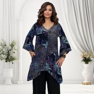 May include: A dark blue tunic with a V-neck and long, flared sleeves. The tunic features a patchwork design with geometric and floral patterns in shades of blue, purple, and green. The model is wearing black trousers.
