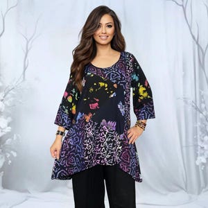 Könnte beinhalten: Ein schwarzes Tunika-Oberteil mit Rundhalsausschnitt und Dreiviertelärmeln. Das Oberteil hat ein farbenfrohes Batikmuster mit floralen und abstrakten Designs in Lila, Gelb und Rosa. Das Model trägt eine schwarze Hose.