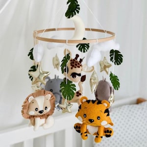 May include: A wooden baby mobile with a white crescent moon, clouds, stars, and felt animal toys including a lion, tiger, giraffe, and elephant. The mobile is hanging from a white ceiling.