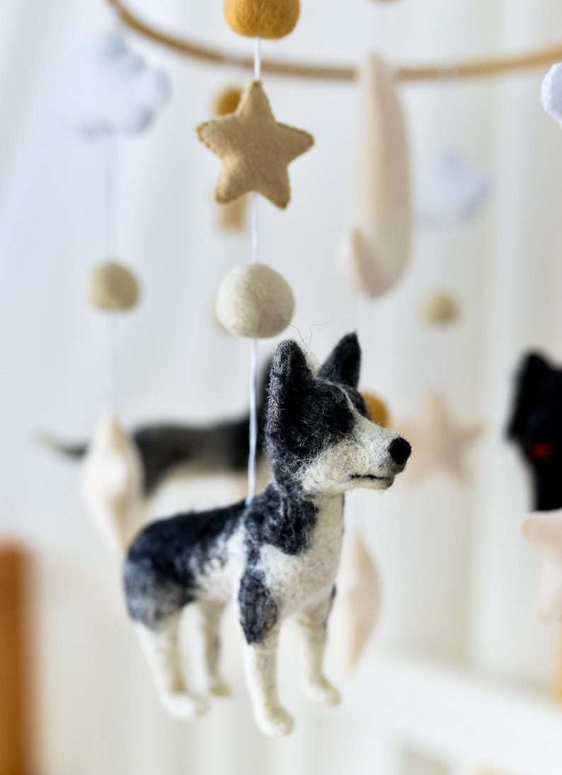 May include: A baby mobile with felt dog figures in black, white, and grey. The mobile also features felt stars, clouds, and spheres in neutral colours, suspended from a wooden hoop.