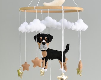 May include: A baby mobile featuring a black and tan dog, white clouds, and gold and brown stars suspended from a wooden hoop. A cream-colored crescent moon sits atop the mobile, creating a whimsical nursery decoration.