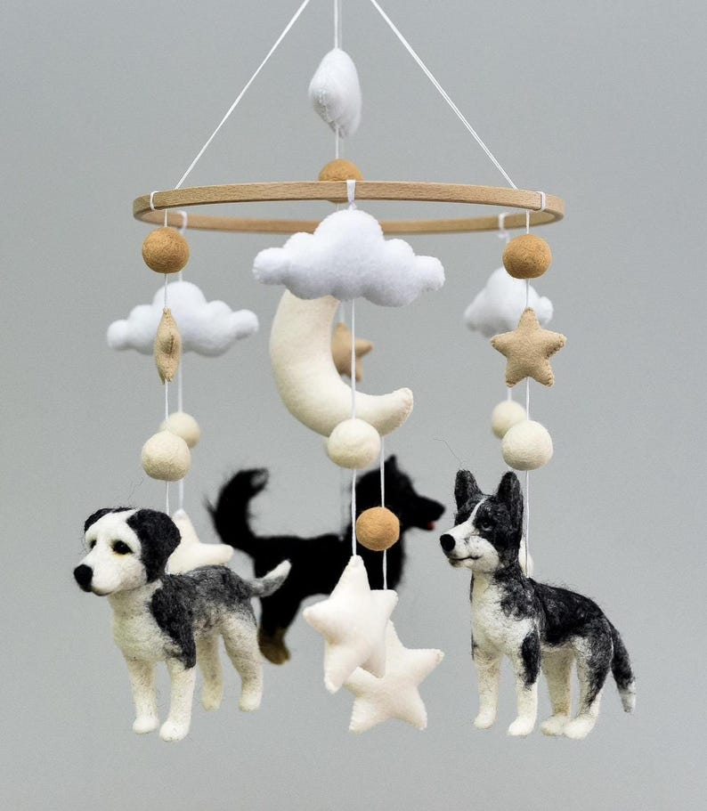 May include: A handmade baby mobile with felt dogs, stars, clouds, and a crescent moon. The mobile has a wooden ring and is suspended by white strings. The dogs are black and white, and the stars and clouds are white.