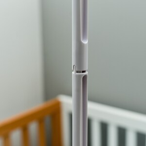 May include: Close-up of a white plastic pole with a telescoping design. The pole is made of two sections that slide together. The pole is designed to be adjustable in length.