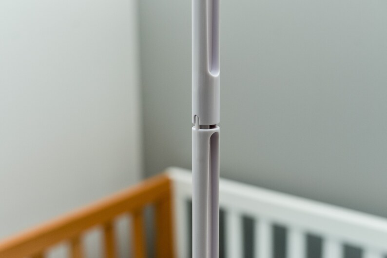 May include: Close-up of a white plastic pole with a telescoping design. The pole is made of two sections that slide together. The pole is designed to be adjustable in length.