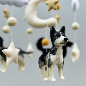 May include: A baby mobile featuring felted dog figures in black and white, along with stars, moons, and clouds. The nursery decor is suspended by white strings, creating a whimsical and gentle atmosphere.