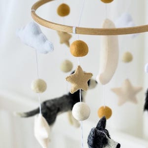 May include: A baby mobile with felted dogs, stars, clouds, and spheres in neutral tones. The wooden hoop suspends the hanging elements. The dogs are black and white, and the stars are tan.