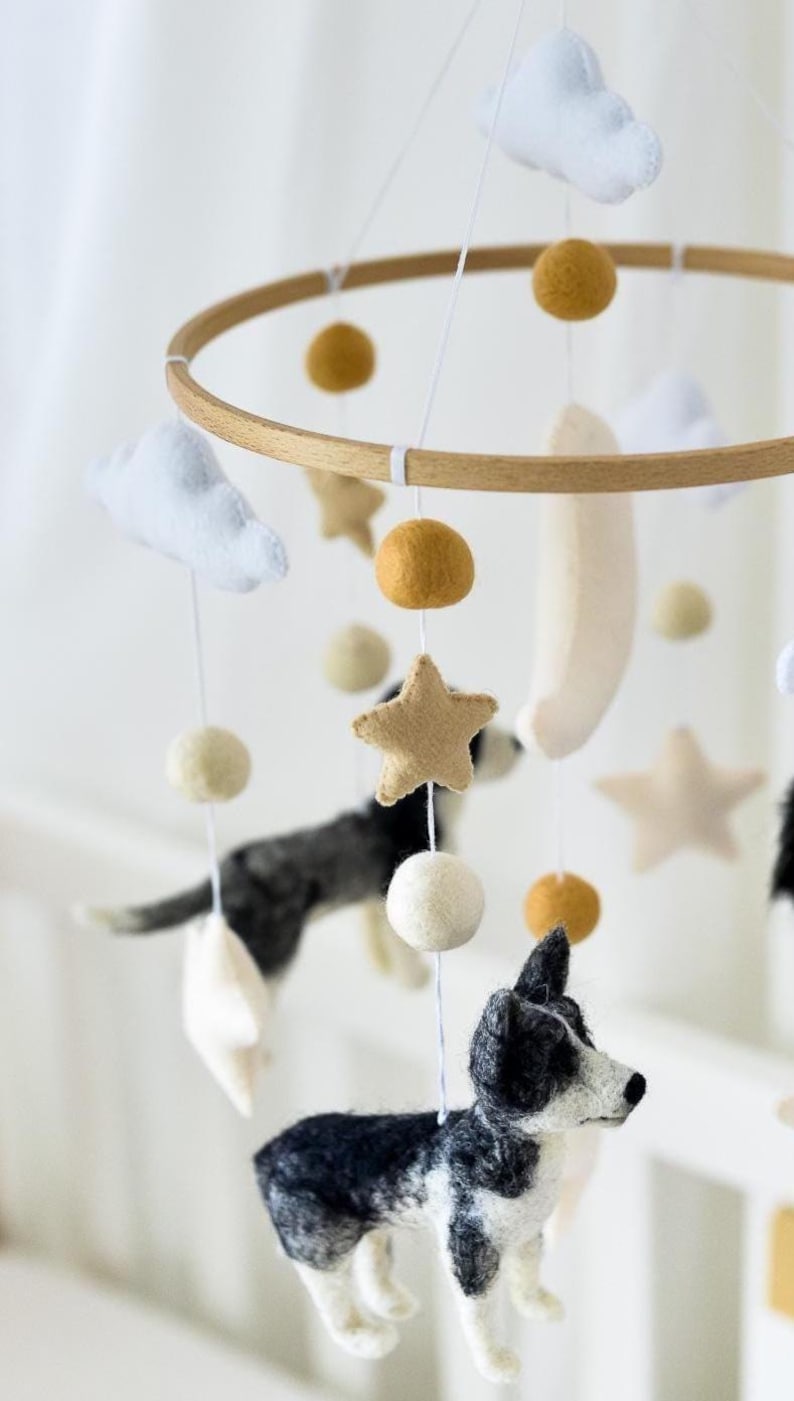 May include: A baby mobile with felted dogs, stars, clouds, and spheres in neutral tones. The wooden hoop suspends the hanging elements. The dogs are black and white, and the stars are tan.
