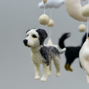 May include: A handmade baby mobile with felted dog figures in black, white, and grey. The mobile includes a crescent moon, clouds, and hanging spheres. The dog figures are the focal point of this nursery decor.