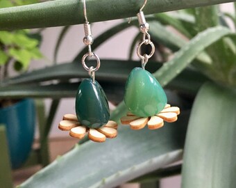 May include: A pair of green agate stone earrings with a wooden flower design. The earrings are on a green plant stem.