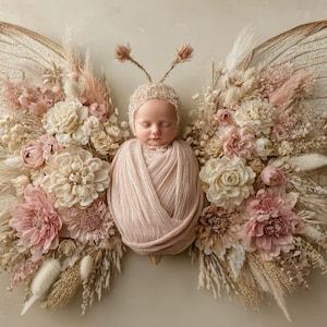 May include: A newborn baby wrapped in a pink blanket, wearing a matching bonnet, and nestled within a floral butterfly arrangement. The arrangement features cream, pink, and beige flowers and dried grasses, with large butterfly wings in the background.