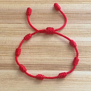 Op de afbeelding: Een rood touw armband met geknoopte kralen. De armband is in een figuur acht geknoopt.