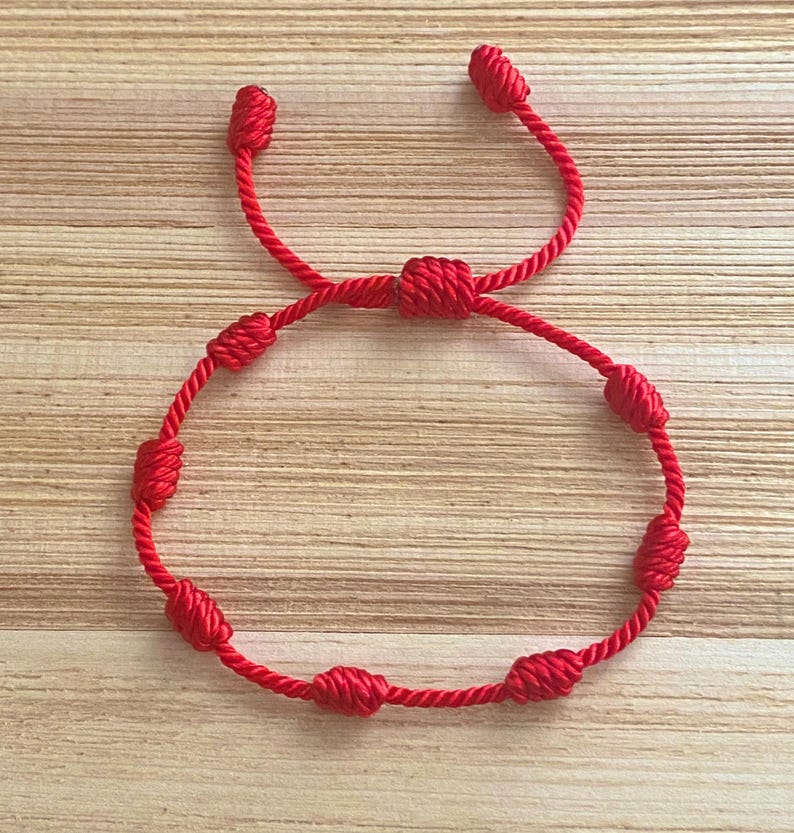Op de afbeelding: Een rood touw armband met geknoopte kralen. De armband is in een figuur acht geknoopt.