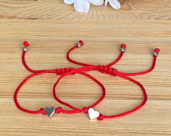 May include: Three red string bracelets with silver heart charms. The bracelets are tied together in a knot.