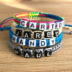 May include: Four colorful friendship bracelets with black letter beads spelling out the names Carter, Jared, Mandy, and Paul.