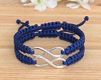 May include: Two navy blue friendship bracelets with an infinity symbol charm. The bracelets are made of braided cord and are tied together with a knot.