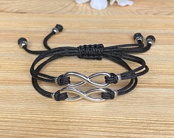 May include: Two black string bracelets with silver infinity symbol charms. The bracelets are tied together with a knot.