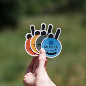 May include: A set of four circular stickers featuring a black antenna graphic and the text BALANCED Dog owner. The stickers are colored in orange, yellow, olive green, and light blue, each with a white border and a black curved line at the bottom.