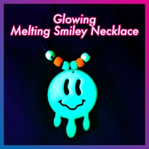 May include: A glowing, turquoise "Melting Smiley Necklace" with a black cord. The pendant features a dripping smiley face design. The necklace has green and orange beads. The text "Glowing Melting Smiley Necklace" is in pink.