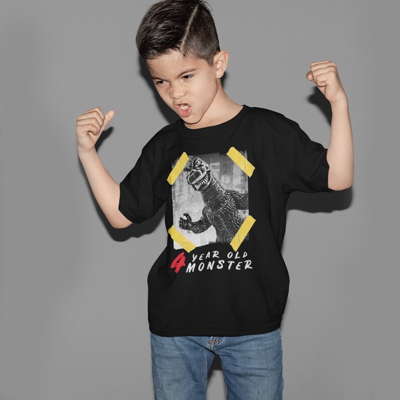 May include: A black t-shirt with a graphic of a monster in a yellow frame. The text "4 year old monster" is printed on the shirt in red and white.