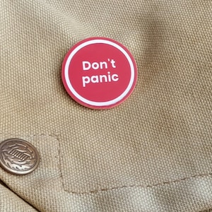 May include: A red circular button with white text that reads "Don't panic" on a beige fabric background.