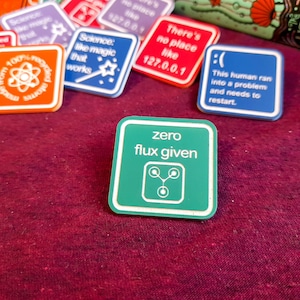 May include: A green square pin with white text that reads "zero flux given". The pin has a stylised image of a three-pronged atom inside a circle.