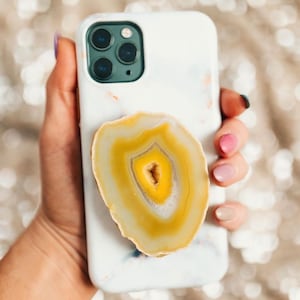 May include: White phone case with a marble pattern and a yellow agate stone glued to the back.