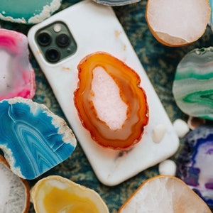 May include: A white iPhone with a clear case and a variety of agate slices in different colors and patterns. The agate slices are arranged around the phone and some are on top of the phone.