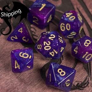 May include: A set of seven purple and blue dice with gold glitter and gold numbers. The dice are on a wooden surface.