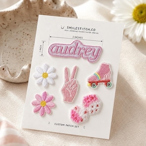 May include: A custom patch set on a white display card featuring the text SMILESTITCH.CO and PSST. SOMEONE THINKS YOU'RE SPECIAL. The patches include the name Audrey, a white daisy, a pink peace sign, a pink roller skate, a pink flower, and dice.