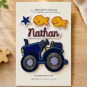 May include: A custom patch set on a display card featuring a dark blue tractor, the name Nathan in brown script, two yellow fish, and a dark blue star. The card includes the text SMILESTITCH.CO and states the tractor is 3 in (W) x 2 in (H).