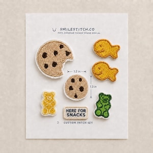 May include: A custom patch set on a white card featuring a large chocolate chip cookie, a smaller cookie, two fish-shaped crackers, a yellow gummy bear, a green gummy bear, and a rectangular patch with the text HERE FOR SNACKS. The smaller cookie measures 1.2 inches.