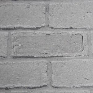 May include: A close-up of a white brick wall with a rectangular, clear plastic plate mounted on the wall.