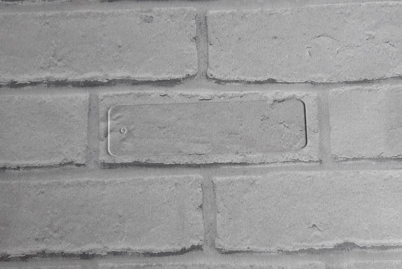 May include: A close-up of a white brick wall with a rectangular, clear plastic plate mounted on the wall.