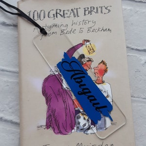 May include: A book titled "100 Great Brits: A rhyming history from Bede to Beckham" by James Muirden. A blue bookmark with the word "Always" written in white is placed on the book.