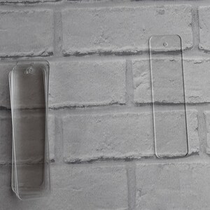 May include: Two clear acrylic bookmark blanks, one is stacked on top of the other. The blanks are rectangular and have a hole at the top for hanging.