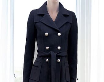May include: A woman wearing a dark blue double-breasted peacoat with silver buttons and a matching belt. The coat has two flap pockets on the front and a cinched waist.