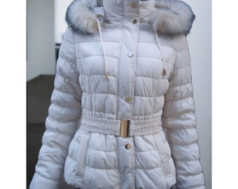 May include: A white puffer jacket with a faux fur hood and a belt. The jacket has a zipper closure and a button closure. The jacket is quilted and has a fitted silhouette.
