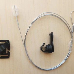 May include: A black plastic cable clip with a silver cable attached to it. The cable is looped and has a small brush on the end. There is also a black plastic mount with a hook on it.