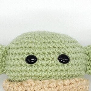 May include: A crocheted green plush toy with black eyes and a tan crocheted scarf.