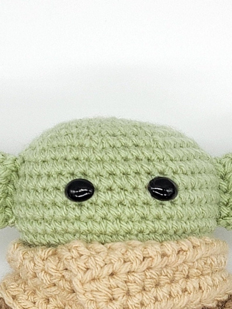 May include: A crocheted green plush toy with black eyes and a tan crocheted scarf.