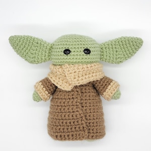 May include: A crocheted green and brown plush toy with large ears and black eyes. The toy is wearing a brown robe with a tan collar.
