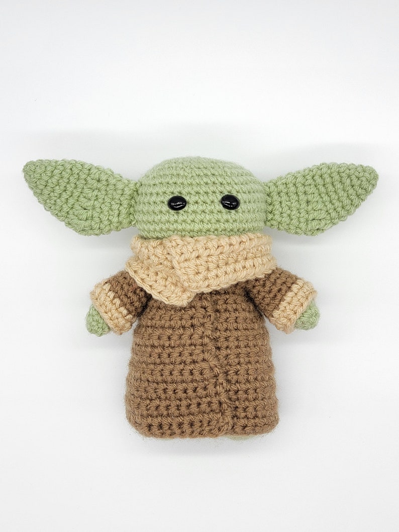 May include: A crocheted green and brown plush toy with large ears and black eyes. The toy is wearing a brown robe with a tan collar.